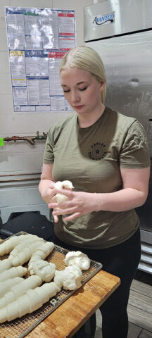 General Manager, Emilee Davis making doughnuts in the back